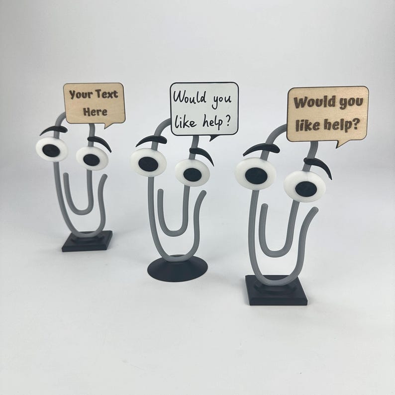May include: Three whimsical paper clip desk organizers with googly eyes and speech bubbles. One bubble reads "Your Text Here," and two say "Would you like help?" The clips are gray, with black bases.