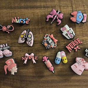 May include: A collection of colorful nurse-themed charms. The charms include a stethoscope, lungs, a syringe, a nurse's uniform, and the word "Nurse" in various designs. Some charms have the text "Nurse Life" and "Nurse Off Duty".