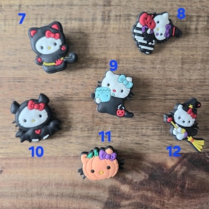 May include: A selection of Halloween-themed shoe charms featuring Hello Kitty. The charms depict Hello Kitty in various costumes, such as a witch, bat, and cat, with bright colours and detailed designs.