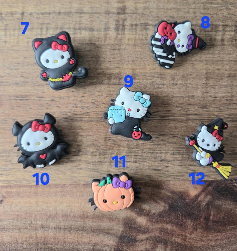 May include: A selection of Halloween-themed shoe charms featuring Hello Kitty. The charms depict Hello Kitty in various costumes, such as a witch, bat, and cat, with bright colours and detailed designs.