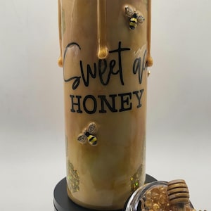 May include: A tall, cylindrical tumbler with a honey-themed design. The tumbler features a dripping honey effect, the words "Sweet as Honey", and decorative bee accents. The lid is off, revealing a honey dipper and honey-like beads.