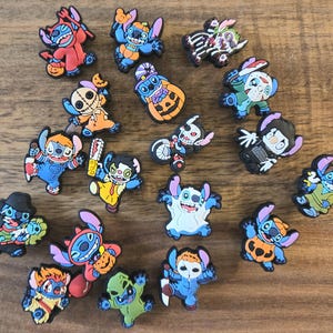 May include: A selection of colourful shoe charms featuring a blue alien-like cartoon character in various Halloween costumes. The charms include a vampire, ghost, and pumpkin. The rubber charms are designed to be attached to shoes.