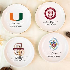 Può includere: Quattro piattini rotondi in ceramica bianca con bordi dorati. Ogni piatto presenta un logo universitario e un nome con "Classe 2025". Un piatto ha il logo dell'Università di Miami, un altro quello dell'Università di Chicago.