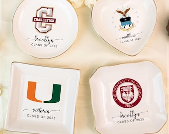 Puede incluir: Cuatro platitos de cerámica blanca con bordes dorados. Cada plato presenta un diseño diferente: un plato redondo con "Charleston", un plato en forma de corazón con un escudo, un plato cuadrado con "Miami" y un plato festoneado con "University of Chicago".
