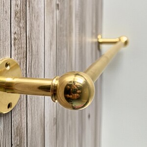 Side-angle view of solid brass towel bar on rustic wood wall, unlacquered finish.