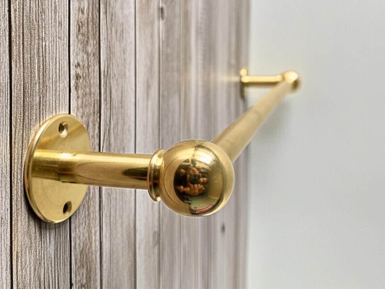 Side-angle view of solid brass towel bar on rustic wood wall, unlacquered finish.