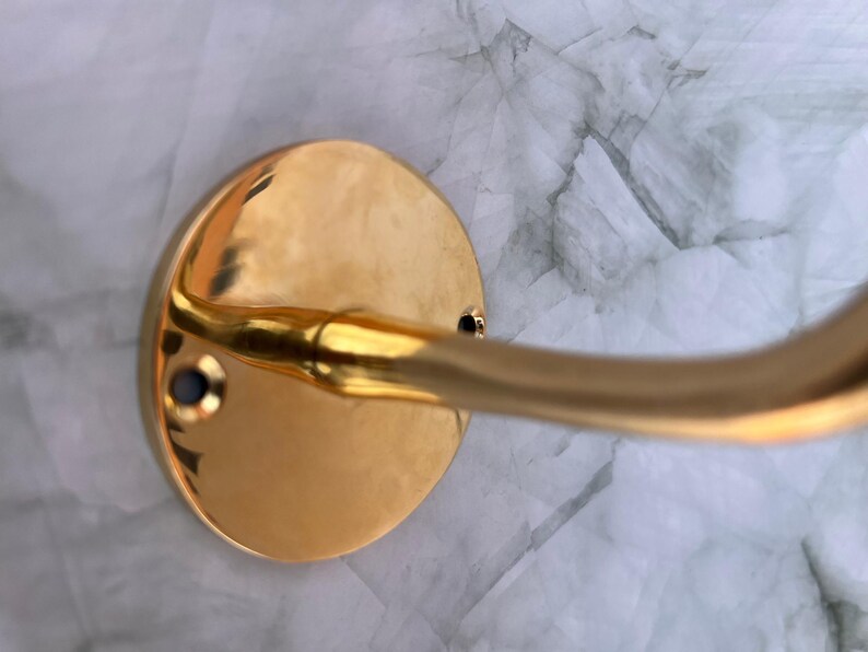 Close-up of brass hook base and screws mounted on marble wall.