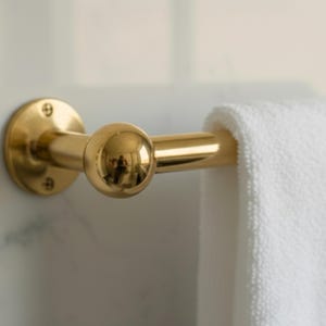 Close-up of brass towel bar end with round mount and towel draped, Moroccan craftsmanship.