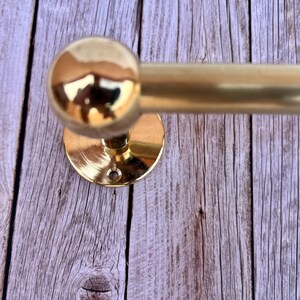 Close-up detail of brass towel holder mount plate against wood wall, polished unlacquered brass.