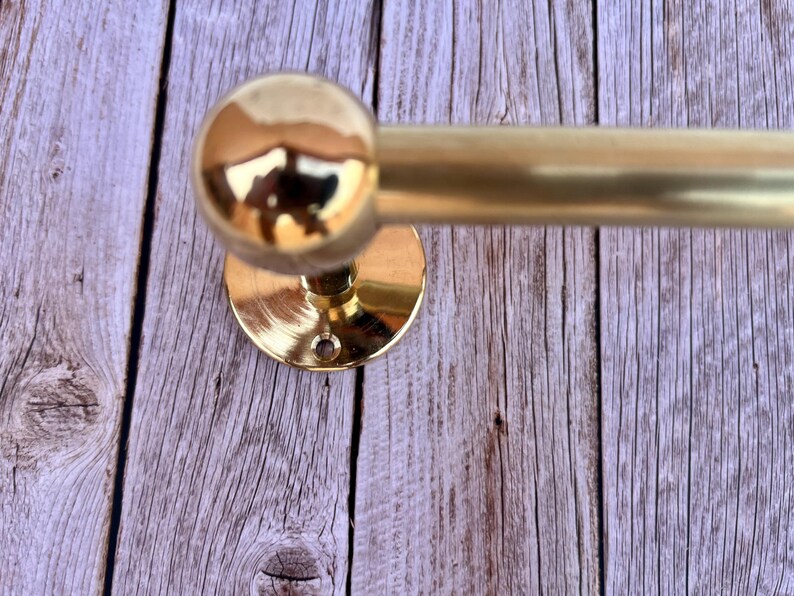 Close-up detail of brass towel holder mount plate against wood wall, polished unlacquered brass.