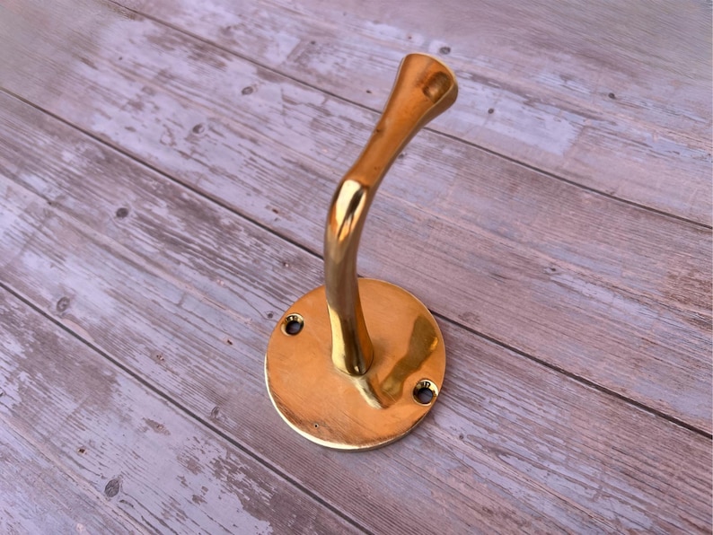 Angled view of brass wall hook mounted on wooden wall.