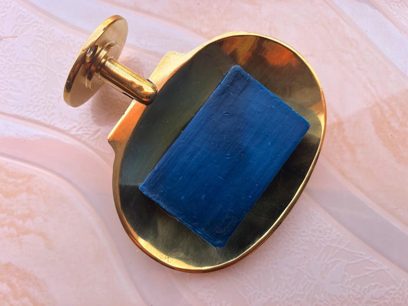 Brass wall mounted soap dish holding blue bar soap, handmade bathroom accessory.