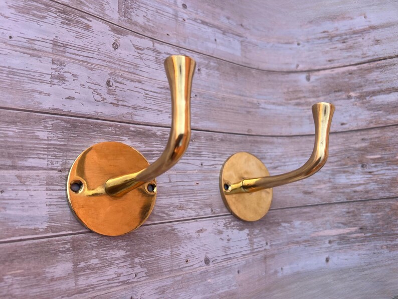 Set of two unlacquered brass wall hooks mounted on wood panel.