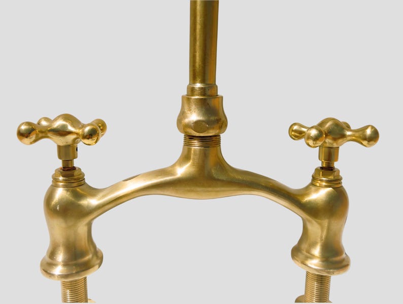 Close-up of solid brass bridge faucet body with cross handles, highlighting artisan craftsmanship and smooth unlacquered finish.