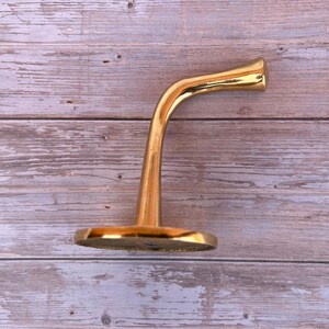 Side profile of solid brass wall hook on wood background.