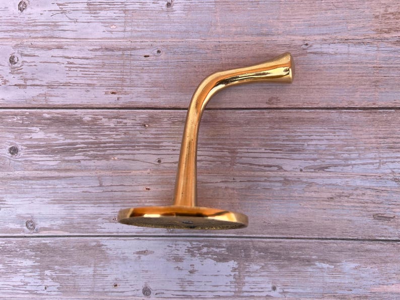 Side profile of solid brass wall hook on wood background.