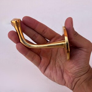 Hand holding brass wall hook against white background.