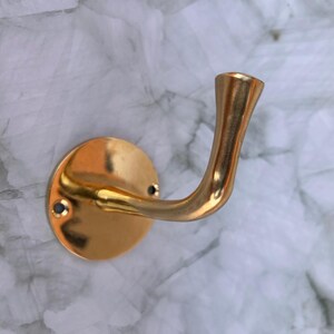 Single brass wall hook fixed on marble wall background.