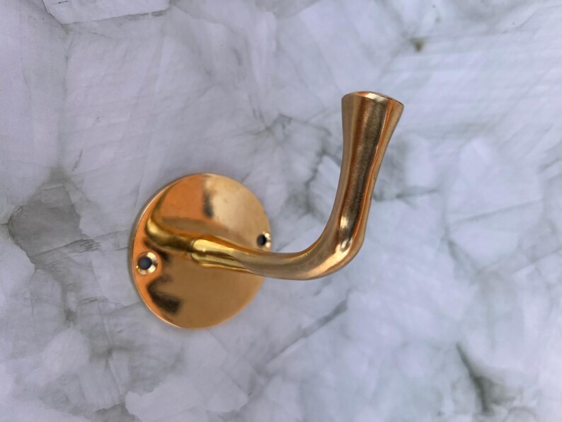 Single brass wall hook fixed on marble wall background.