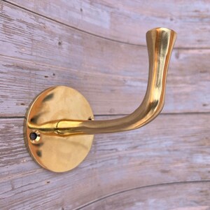 Brass wall hook close-up on rustic wooden wall background.
