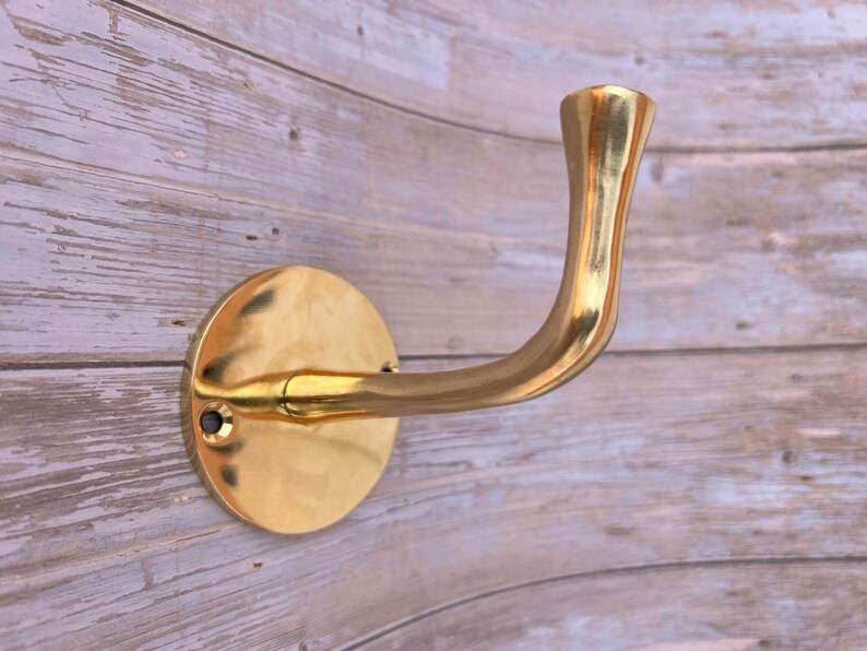 Brass wall hook close-up on rustic wooden wall background.