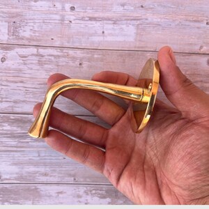 Hand holding handmade brass wall hook for scale.