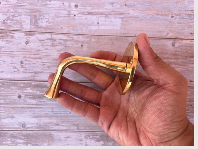 Hand holding handmade brass wall hook for scale.
