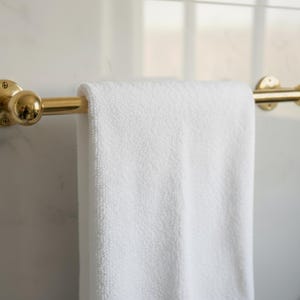 Handmade brass towel bar holding towel, polished unlacquered finish, wall-mounted on marble.
