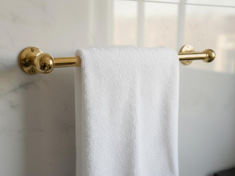 Handmade brass towel bar holding towel, polished unlacquered finish, wall-mounted on marble.