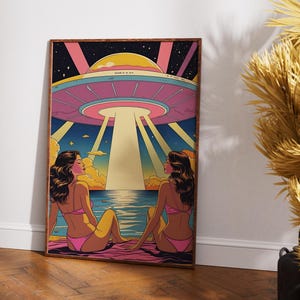 Könnte beinhalten: Ein gerahmter Kunstdruck mit einer Retro-Illustration von zwei Figuren in rosa Badekleidung an einem Strand, die ein schwebendes UFO betrachten. Das Kunstwerk verwendet Rosa, Gelb, Blau und Schwarz mit einem sternenklaren Nachthimmel. Der Druck ist in einem Holzrahmen.