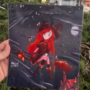 May include: A print featuring a cartoon witch with long red hair, a black hat, and a black cat, riding a broom through a starry night sky. The artwork includes a castle and the text "Angel Draws".
