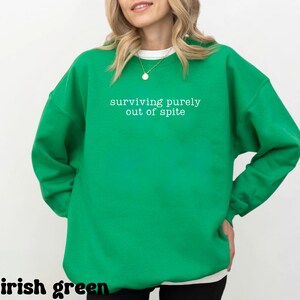 May include: Irish green sweatshirt with the text "surviving purely out of spite" in white. The sweatshirt has a crew neck and long sleeves. The words "irish green" are at the bottom of the image.