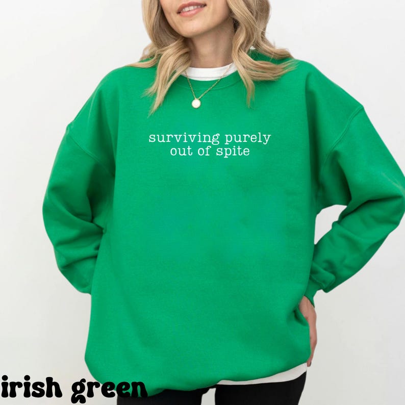 May include: Irish green sweatshirt with the text "surviving purely out of spite" in white. The sweatshirt has a crew neck and long sleeves. The words "irish green" are at the bottom of the image.