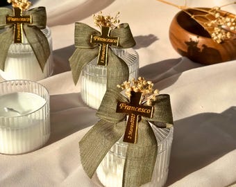 Puede incluir: Candelabros de vidrio transparente con velas blancas, adornados con cintas verde oliva y dijes de cruz dorados. Los dijes dicen "Francesco" y "2 Marzo 2023". Flores secas coronan cada vela, creando un regalo elegante y personalizado.