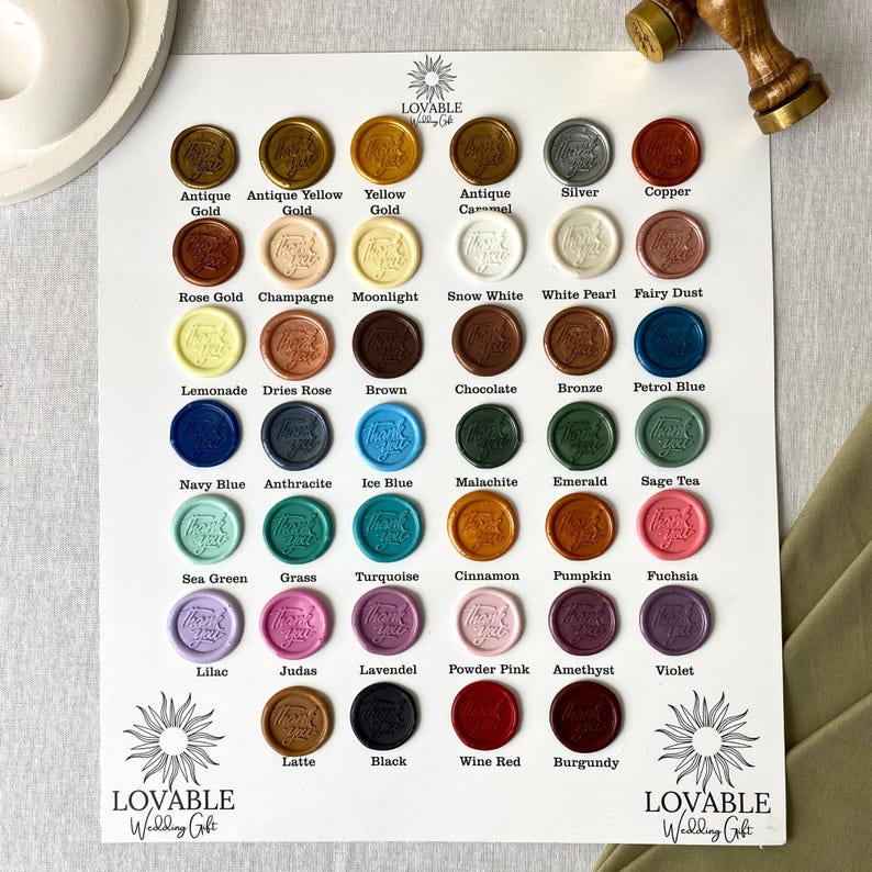 Puede incluir: Una variedad de sellos de cera de colores, en tonos dorados, plateados, cobrizos y otros colores. Cada sello est&aacute; etiquetado con su nombre de color, como "Rose Gold", "Navy Blue" y "Fuchsia". El texto "LOVABLE Wedding Gift" es visible.