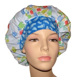 May include: A blue and white surgical scrub hat with a pattern of footprints and handprints. The hat is made of a soft, comfortable fabric and is perfect for nurses, doctors, and other healthcare professionals.