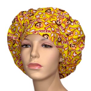 May include: Yellow surgical scrub hat with a repeating pattern of cartoon faces, bones, and the words "Operation" in red.