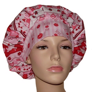 May include: A pink and red bouffant scrub cap with a Valentine's Day theme. The cap features hearts, ladybugs, and the words "Kiss me" and "Love" printed on it. The cap is designed to be worn in a medical or beauty setting.
