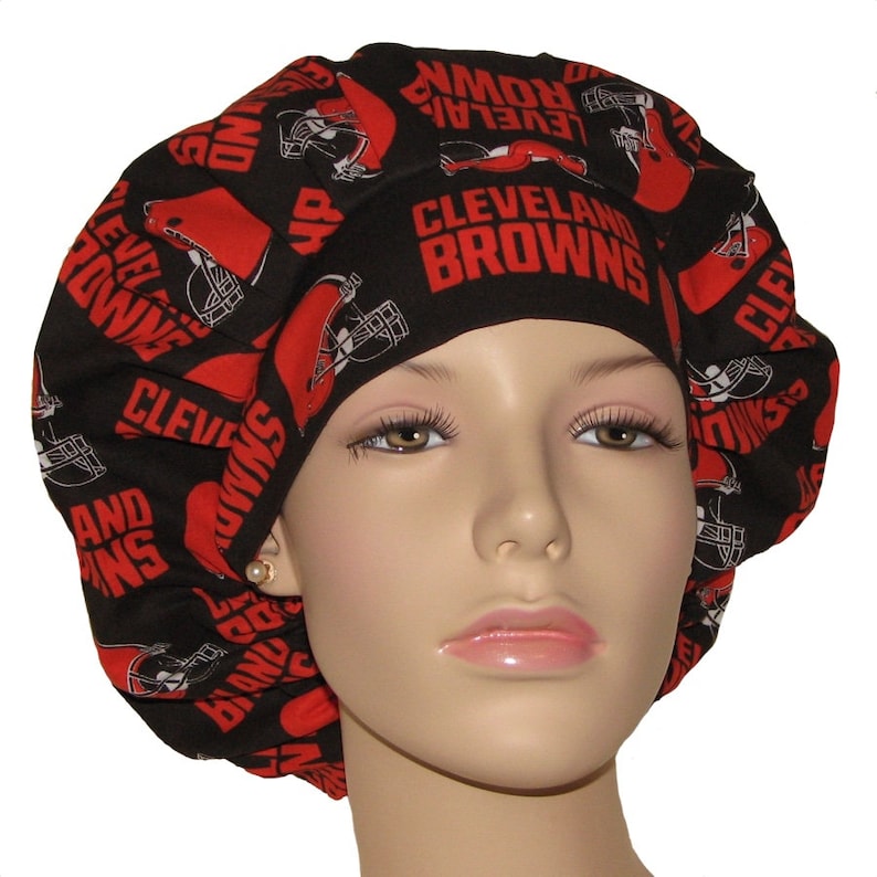 May include: Black scrub hat with a red and white print of the Cleveland Browns logo and helmets.
