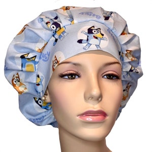 May include: Blue surgical scrub hat with a cartoon dog print featuring the words "Bluey" and "Bingo".