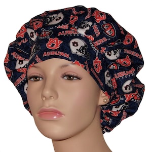 May include: A navy blue scrub cap featuring the Auburn University logo and the word "AUBURN" in orange and white. The cap has a repeating pattern of the team's logo and text. The cap is designed to cover the head and hair.