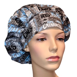 May include: Gray and blue surgical scrub hat with a print of eye-related medical terms in black and white. The text includes words like "iris", "cones", "cataracts", and "opthalmologist".