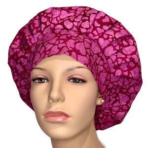 May include: A pink surgical scrub hat with a heart pattern. The hat is made of a soft, comfortable fabric and is designed to be worn by medical professionals.
