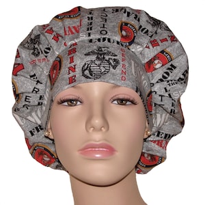 May include: Gray scrub hat with a red, white, and blue design featuring the United States Marine Corps emblem and the words "United States Marine Corps", "Semper Fidelis", "The Few, The Proud", "Defend Freedom", "Courage", "Honor", "Duty", "Commitment", "Integrity", "Service", "Loyalty", "Discipline", and "Excellence".