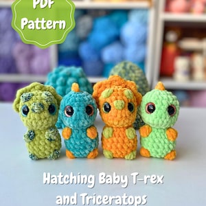 Op de afbeelding: Vier gehaakte babyspeelgoed dinosaurussen in groen, blauw en oranje. De speeltjes hebben grote ogen en zijn gelabeld met "Hatching Baby T-rex and Triceratops". Een groen en wit PDF-patroonlabel staat linksboven.