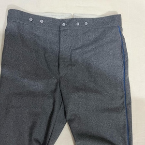 Könnte beinhalten: Graue Wollhose mit blauem Streifen an der Seite. Die Hose hat einen Knopfverschluss und eine hohe Taille. Der Stoff scheint mittelschwer zu sein, geeignet für kühleres Wetter. Die Hose ist wahrscheinlich Vintage oder historisch.