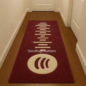 May include: A burgundy rectangular rug with a cream design. The design features horizontal lines and a rounded shape with three curved lines. The text "DecoRugCreations" is visible on the rug. The rug is on a wooden floor.