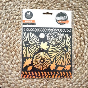 May include: A black stencil mask with a floral and leaf design, featuring the text "STUDIO LIGHT MASKS Grungy bits" and "GRUNGE COLLECTION". The stencil has a variety of patterns and shapes, with orange and yellow gradients.