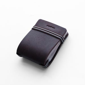 Könnte beinhalten: Ein dunkelbraunes Leder-Notizbuch mit einem passenden Gummiband mit weißen und blauen Streifen. Das Wort "lendhur" ist oben auf dem Notizbuch eingeprägt. Das Notizbuch ist geschlossen.