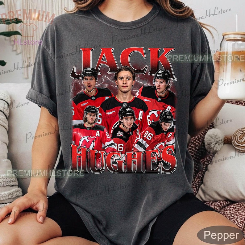 May include: Dark gray t-shirt featuring a graphic of Jack Hughes and other hockey players in red and black jerseys. The name "JACK HUGHES" is printed in red, with a vintage style design.